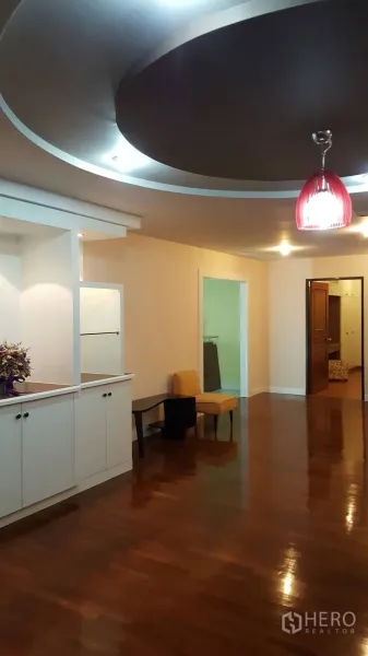 Condominium for rent in Khlong Toei, Bangkok - Hallway and living space with glossy hardwood floors, built-in cabinetry and a feature ceiling with a red pendant light.