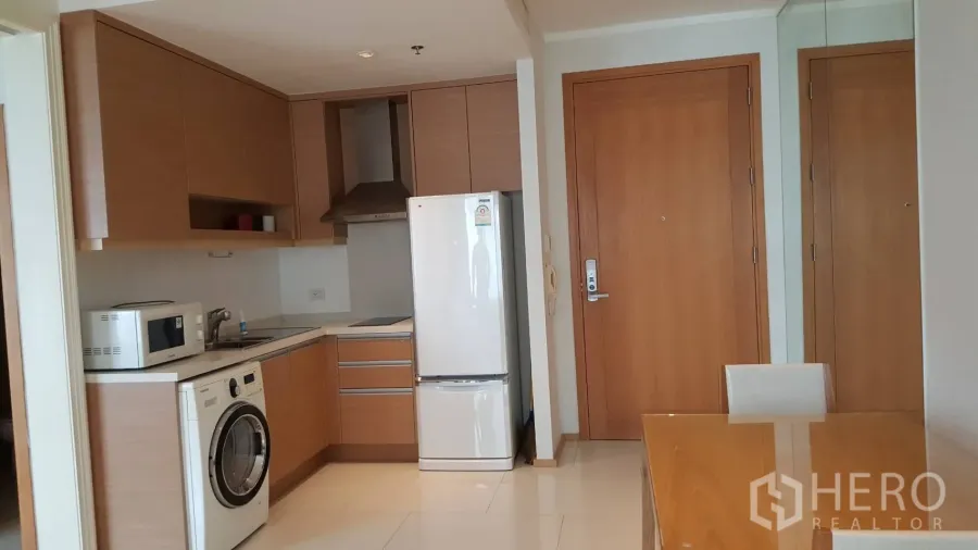 公寓 出租在Khlong Toei, Bangkok - 现代开放式厨房，木质柜体、洗衣机、微波炉与冰箱，旁带用餐区的公寓一角。