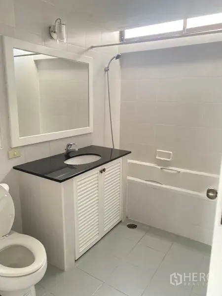 Condominium for rent in Watthana, Bangkok - Clean white bathroom with bathtub and shower over tub plus a vanity with black countertop.