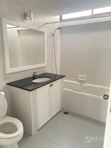Condominium for rent in Watthana, Bangkok - Clean white bathroom with bathtub and shower over tub plus a vanity with black countertop.