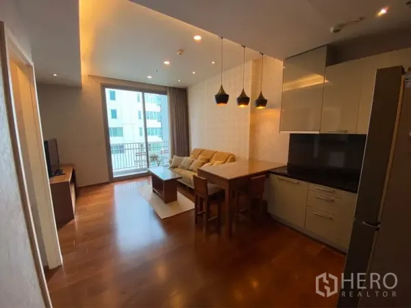 Condominium for rent or sale in Watthana, Bangkok - Open-plan living room with wood floors, modern kitchen, pendant lights and balcony doors in a Thonglor condo.