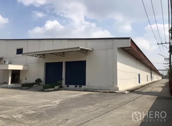 Warehouse for rent in Lam Luk Ka, Pathum Thani - Front facade of industrial warehouse with twin blue roll-up doors and metal awning.