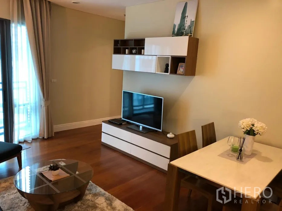 Condominium for rent or sale in Khlong Toei, Bangkok - TV console with wall cabinets beside a two-seat dining table on wooden flooring.