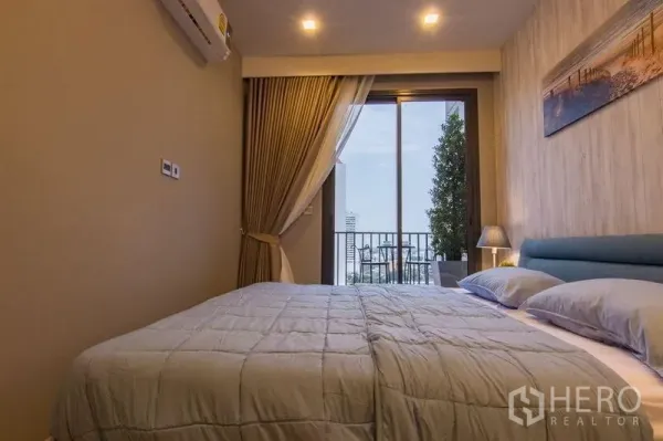 Condominium for sale in Watthana, Bangkok - Cozy bedroom with queen bed and sliding glass door opening to a balcony with city view.