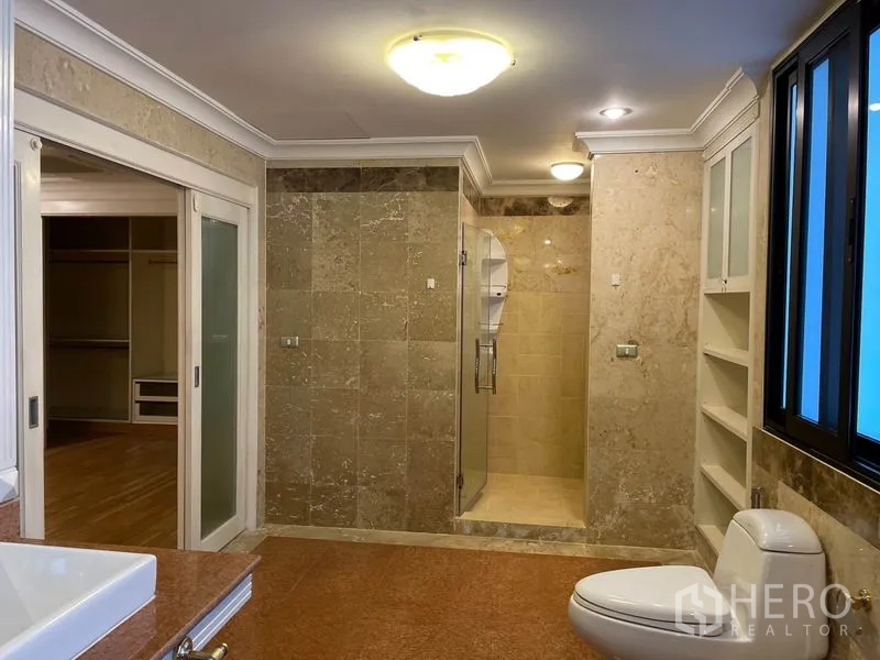 Condominium for rent in Watthana, Bangkok - Spacious bathroom finished in stone with glass shower and built-in shelving.