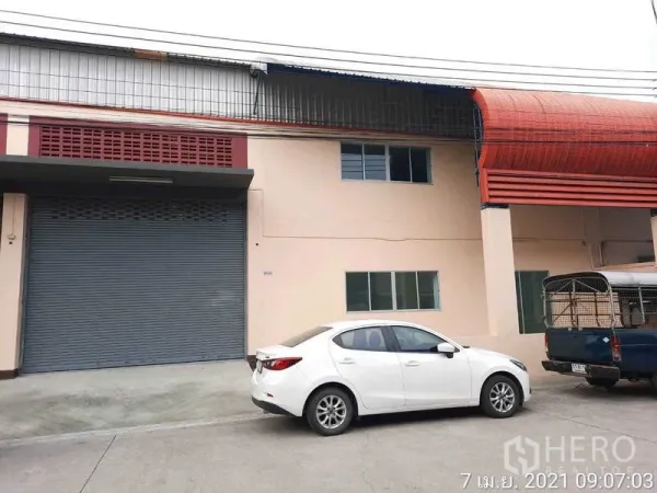 Factory for rent in Bang Bua Thong, Nonthaburi - Factory exterior with large roller shutter, red awning and parking area.
