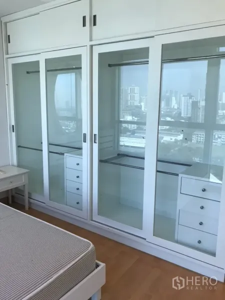 Condominium for rent in Khlong Toei, Bangkok - Bedroom wall of glass-front built-in wardrobes with drawers and skyline reflections.