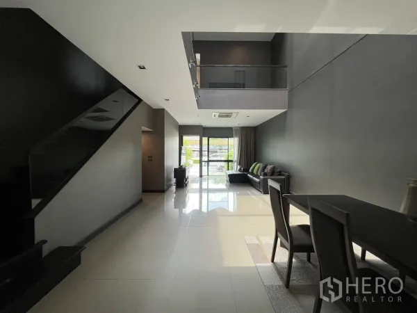 Townhouse for rent in Lat Phrao, Bangkok - Long living space view with staircase, high ceilings and dining table near garden-facing windows.
