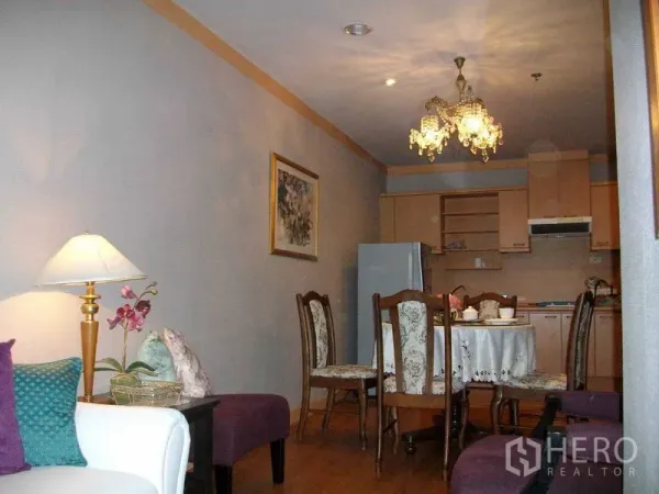 Condominium for rent or sale in Khlong Toei, Bangkok - Open-plan dining and kitchenette with chandelier, wooden cabinets and a round dining table.