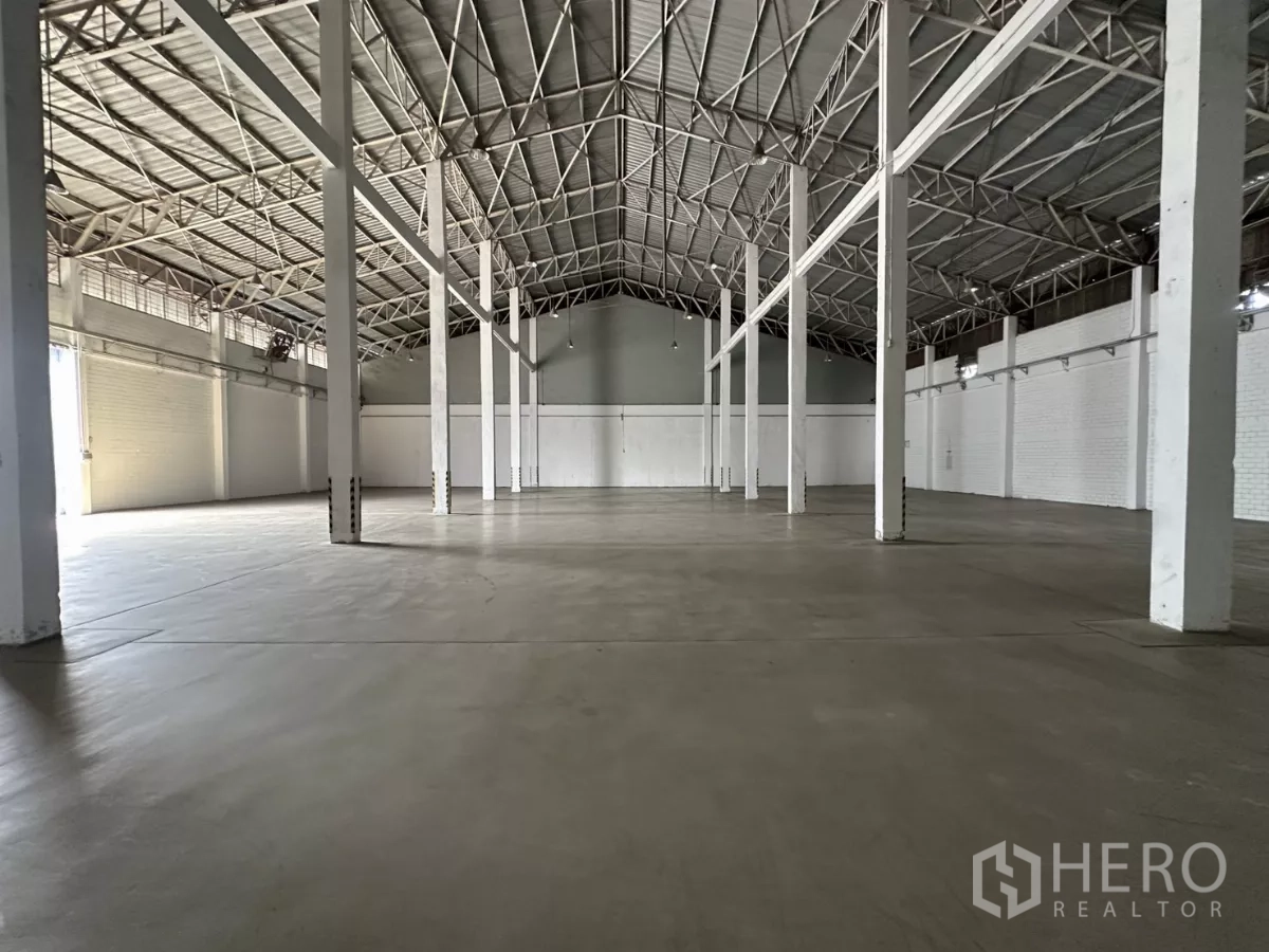 Warehouse for rent in Phra Khanong, Bangkok - Polished concrete floor warehouse space with tall columns and a roller door at the end.