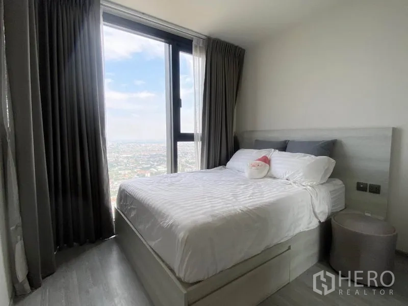 公寓 出租在Phra Khanong, Bangkok - 卧室配大窗与城市景观，双人床铺白色床品。