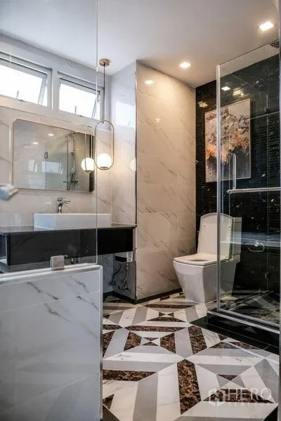 Condominium for rent in Khlong Luang, Pathum Thani - Stylish bathroom with geometric marble tiles, glass shower and floating vanity.