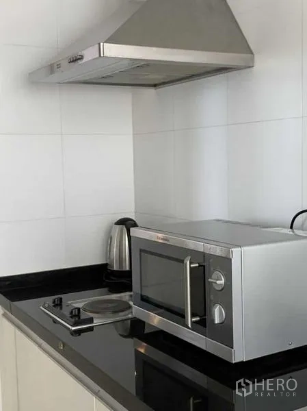 Condominium for rent in Khlong Toei, Bangkok - Close-up of cooktop, microwave, kettle and stainless range hood in the kitchen.