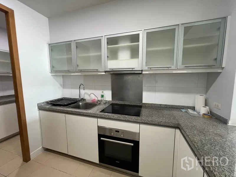 Condominium for rent in Khlong Toei, Bangkok - Modern kitchen with granite countertops, electric hob, oven and glass-front cabinets.
