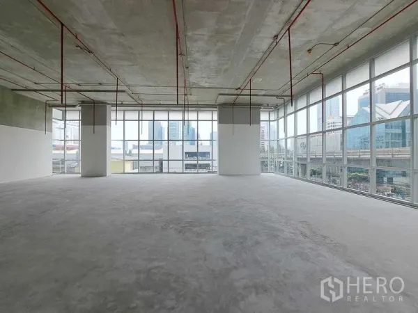 Retail Space for rent in Sathon, Bangkok - Open-plan retail shell with floor-to-ceiling windows, exposed ceiling pipes, concrete floor, and city views beside the BTS line in Sathon, Bangkok.