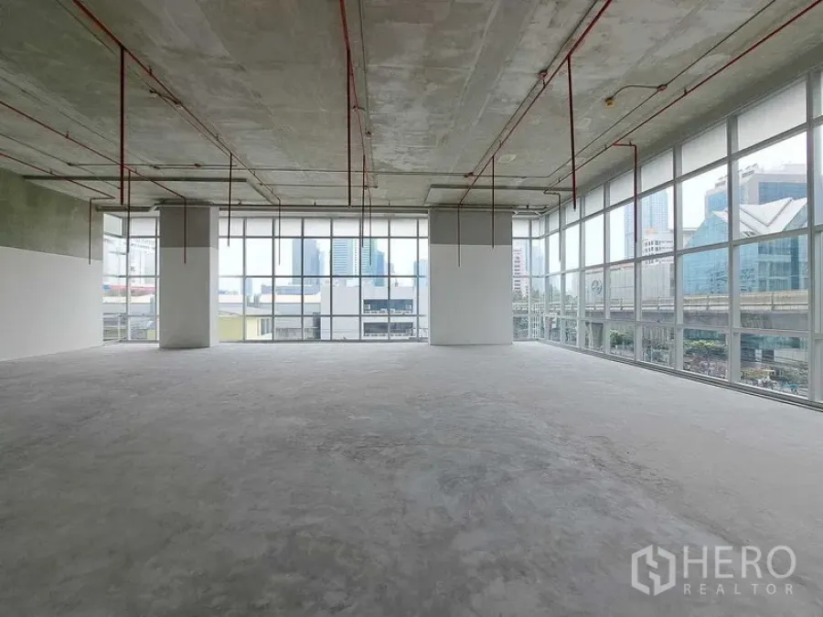 Retail Space for rent in Sathon, Bangkok - Open-plan retail shell with floor-to-ceiling windows, exposed ceiling pipes, concrete floor, and city views beside the BTS line in Sathon, Bangkok.