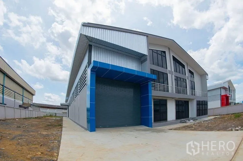 Warehouse for sale in Krathum Baen, Samut Sakhon - Angled exterior view with blue roller shutter loading dock and glass-front offices.