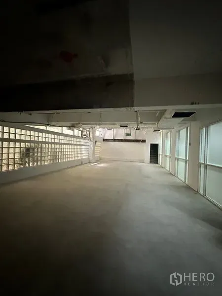 Retail Space for rent - Empty retail space featuring a glass-block side wall, window panels, ducted ceiling and a rear doorway for flexible layout options.