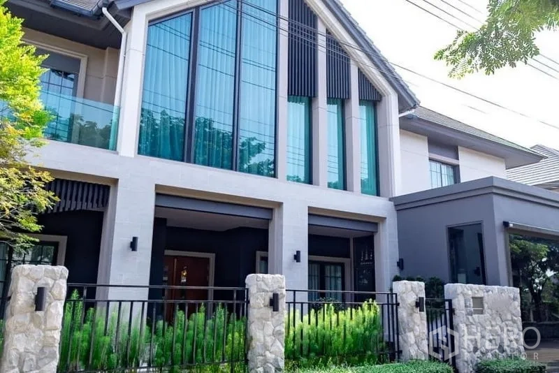 独立式住宅 出售在Pak Kret, Nonthaburi - 暖武里帕克烈现代独栋别墅外立面，高挑玻璃山墙与石质围栏和前庭景观。