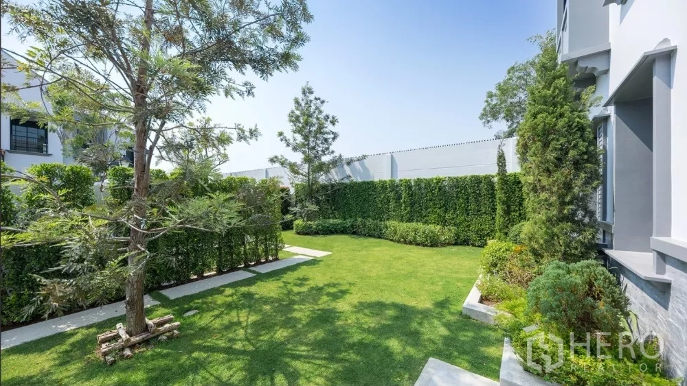 Detached House for rent or sale in Khlong Toei, Bangkok - Landscaped private garden with manicured lawn, hedges and trees beside a modern house.