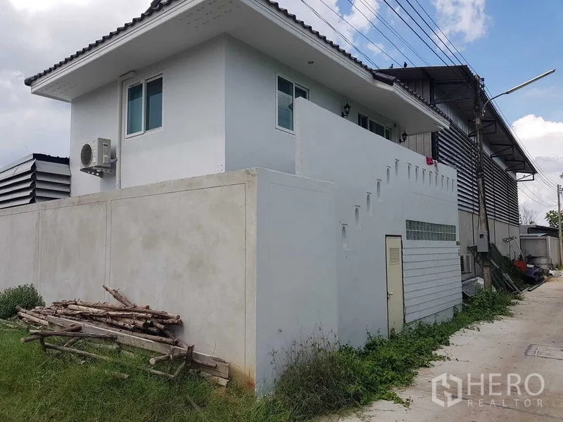 Warehouse for sale in Lam Luk Ka, Pathum Thani - Two-storey staff house or office beside the warehouse, white facade with air-conditioning unit and stair access.
