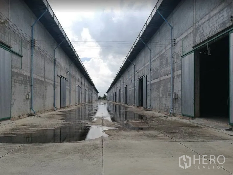 Warehouse for rent in Bang Sao Thong, Samut Prakan - Row of concrete warehouses with a wide driveway, large loading doors and drainage after rain in Bang Sao Thong, Samut Prakan.