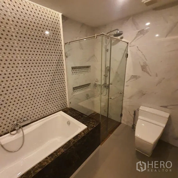 公寓 出租在Bang Kapi, Bangkok - 浴室带浴缸、玻璃淋浴间与图案墙面。