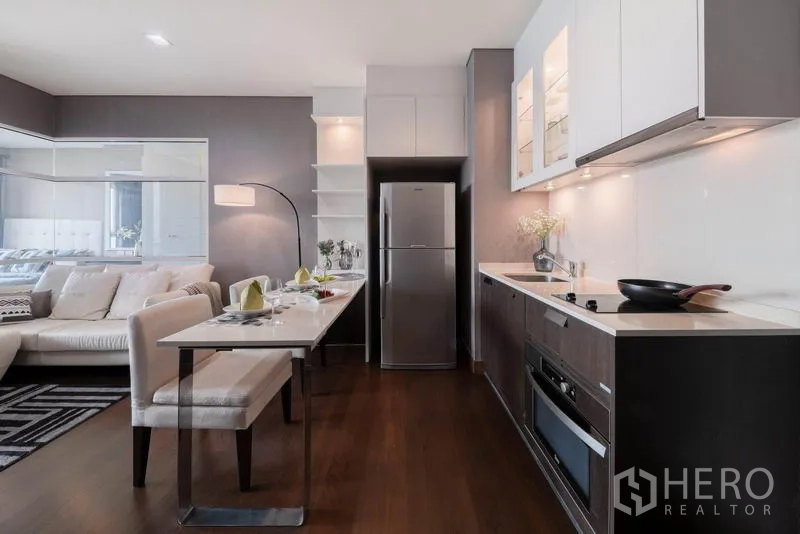 Condominium for rent in Watthana, Bangkok - Modern linear kitchen with built-in appliances, oven, and breakfast table beside the sofa.