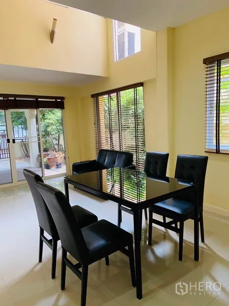 Detached House for rent in Watthana, Bangkok - Dining space with glass-top table, large windows with blinds and access to the patio garden.