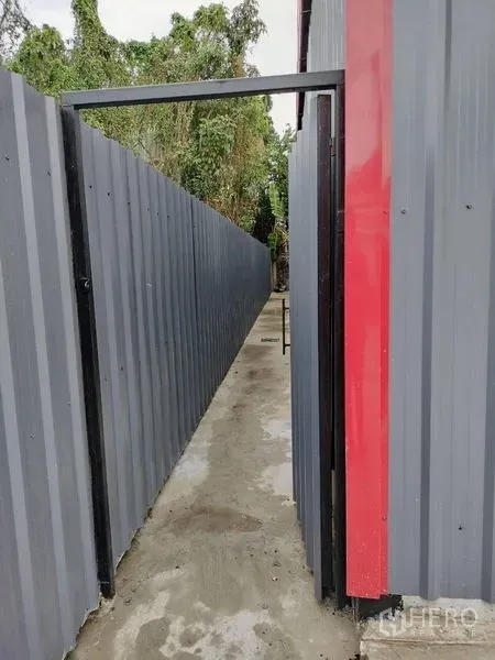 Warehouse for rent in Bueng Kum, Bangkok - Narrow side passage along corrugated metal fencing beside the warehouse leading toward the rear area.