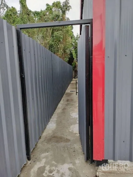 Warehouse for rent in Bueng Kum, Bangkok - Narrow side passage along corrugated metal fencing beside the warehouse leading toward the rear area.