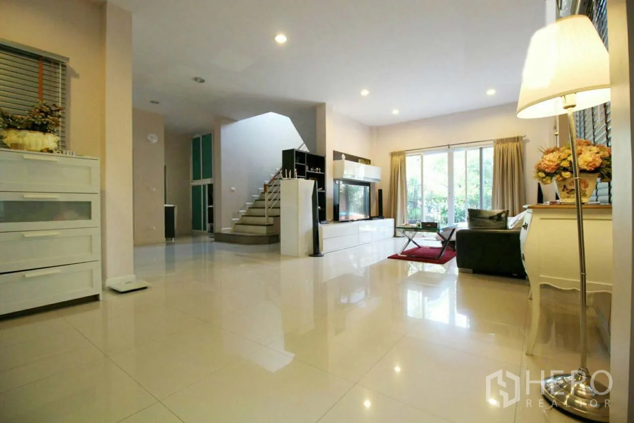 Detached House for rent or sale in Lat Krabang, Bangkok - Spacious living room with glossy tile floors, staircase, TV wall and sliding doors to the garden.