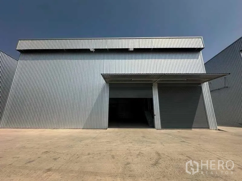 Factory for rent in Wang Noi, Phra Nakhon Si Ayutthaya - Front of a corrugated-metal factory with twin roller shutters and a wide concrete loading apron under a canopy.