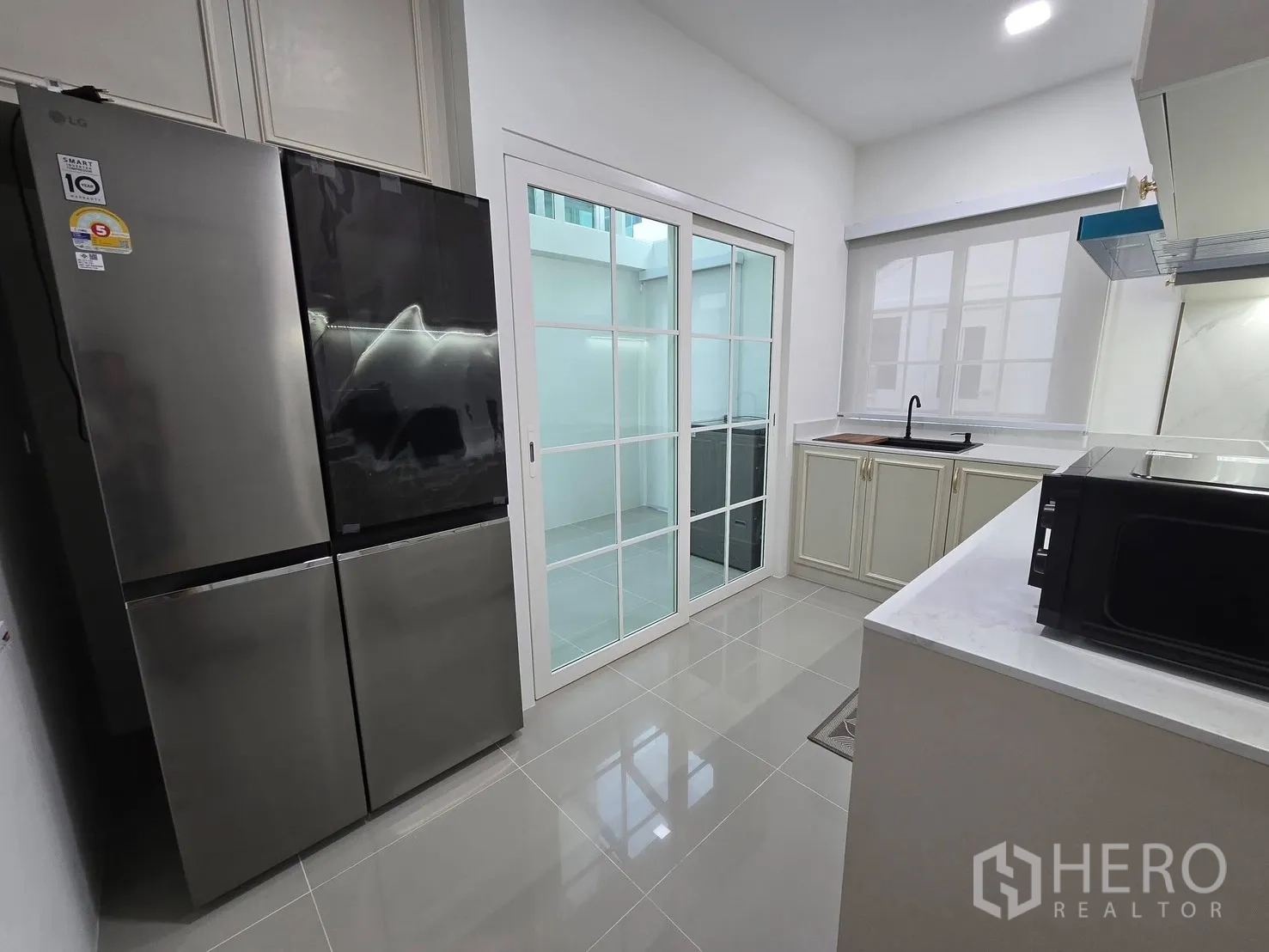 Semi-detached House for rent in Mueang Samut Prakan, Samut Prakan - Enclosed kitchen with sliding glass door, large stainless-steel fridge and white countertops.
