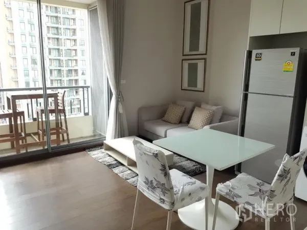 Condominium for rent in Ratchathewi, Bangkok - Open-plan living and dining area with sofa and glass table leading to a balcony with city views.