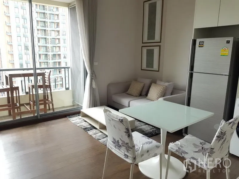 Condominium for rent in Ratchathewi, Bangkok - Open-plan living and dining area with sofa and glass table leading to a balcony with city views.