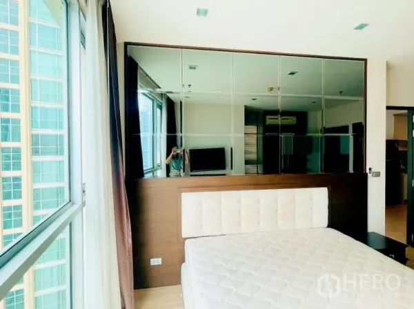 คอนโด ให้เช่า - มุมห้องนอนพร้อมหน้าต่างบานใหญ่และผนังกระจกสะท้อนภายใน