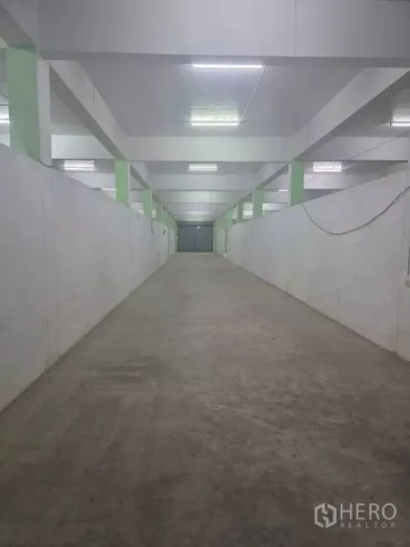 คลังสินค้า ให้เช่าในBang Khun Thian, Bangkok - ทางเดินเก็บของยาว ผนังสีขาว พื้นคอนกรีต มีประตูม้วนท้ายทาง