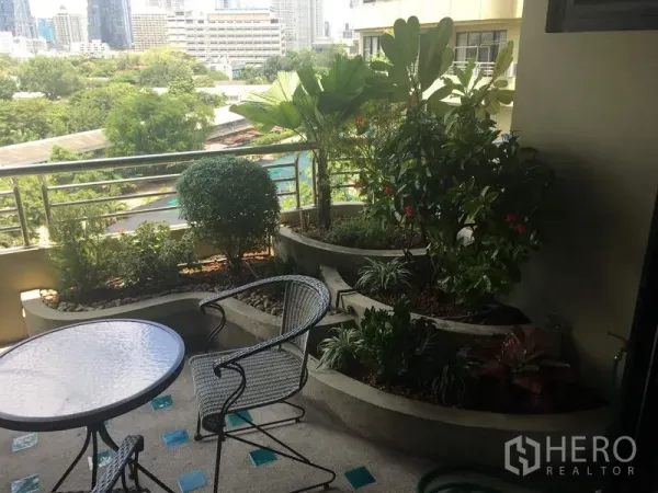 Condominium for rent in Sathon, Bangkok - Balcony with round table and chairs beside built-in planter boxes of lush greenery overlooking the city.