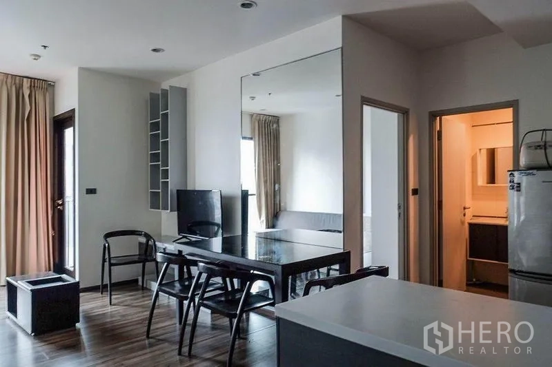 Condominium for rent in Khlong Toei, Bangkok - Dining area with glass table, four chairs and a large wall mirror facing the living room.