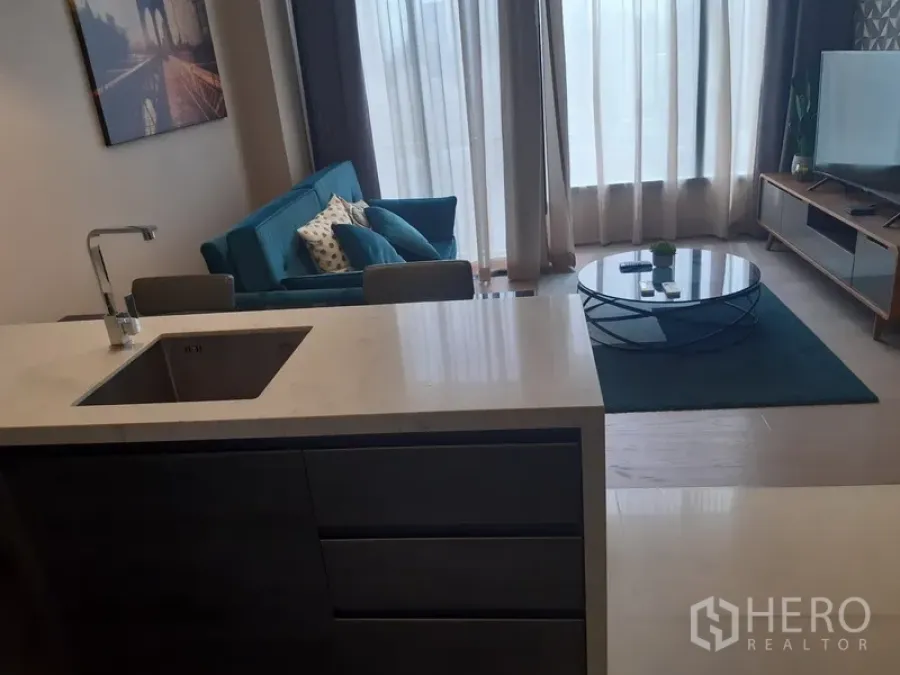 公寓 出租或出售在Watthana, Bangkok - 开放式客厅，青绿色沙发、圆形茶几、电视柜与厨房中岛，落地窗采光充足。