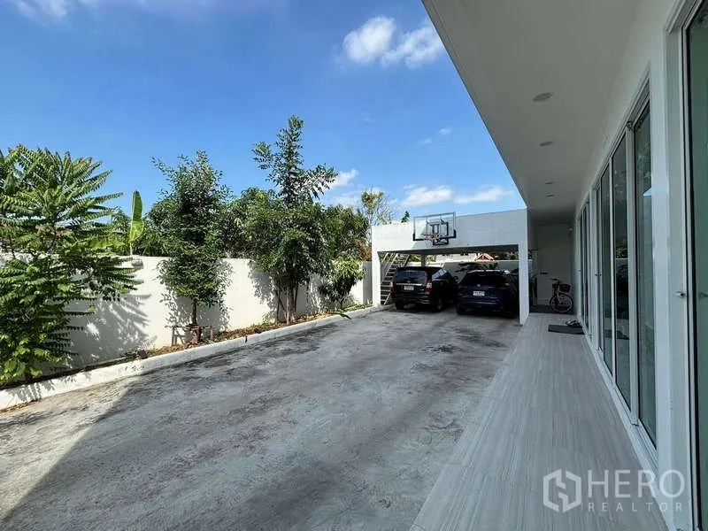 Detached House for rent in Lat Krabang, Bangkok - Private driveway with covered carport, basketball hoop and trees along the wall.