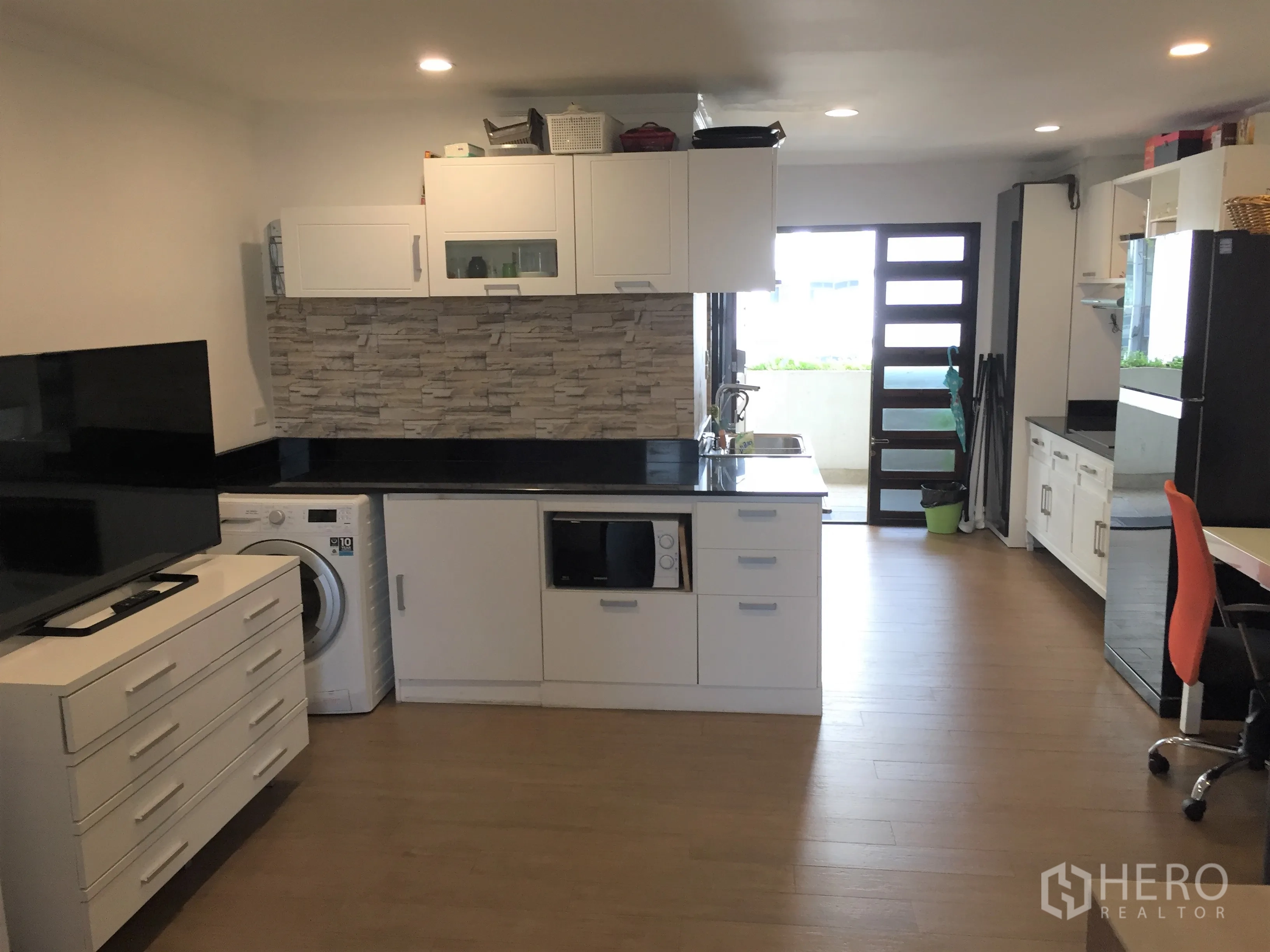 Condominium for rent in Watthana, Bangkok - Modern white kitchen with stone backsplash, black countertops, washing machine, and balcony door.