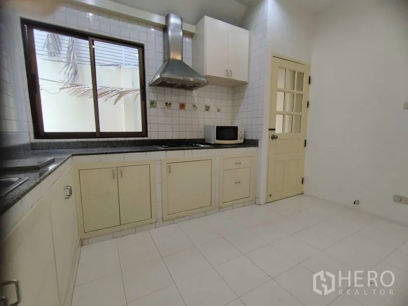 Detached House for rent in Watthana, Bangkok - White tiled kitchen with gas hob, stainless hood, and storage cabinets.