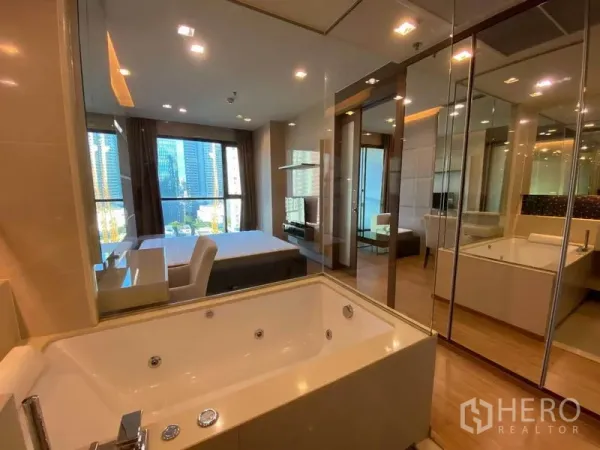 Condominium for rent in Bang Rak, Bangkok - Bathroom with jetted bathtub and mirrored walls looking into the bedroom.