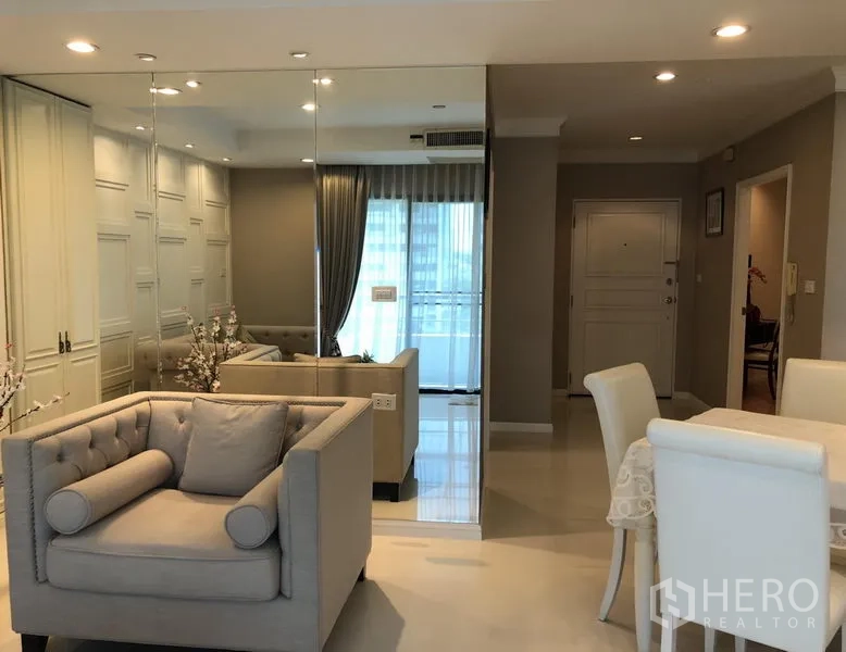 Condominium for rent or sale in Sathon, Bangkok - Open-plan lounge with armchair, full-height mirrored partition, dining area and light from the balcony doors.