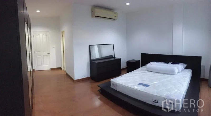 Townhouse for rent in Lat Phrao, Bangkok - Bedroom with platform bed, dresser, air conditioner and white door.