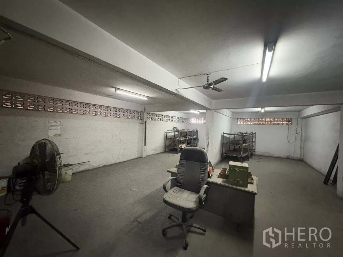Warehouse for rent in Khlong Toei, Bangkok - Ground‑floor workshop space with desks, shelving and an industrial fan.
