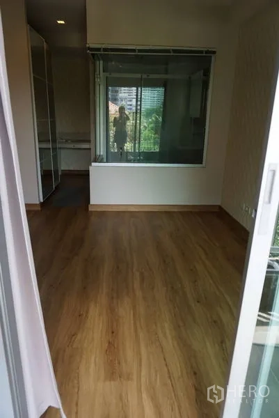 Condominium for sale in Khlong Toei, Bangkok - Bedroom with wood flooring and an interior glass partition, ready for furnishing.