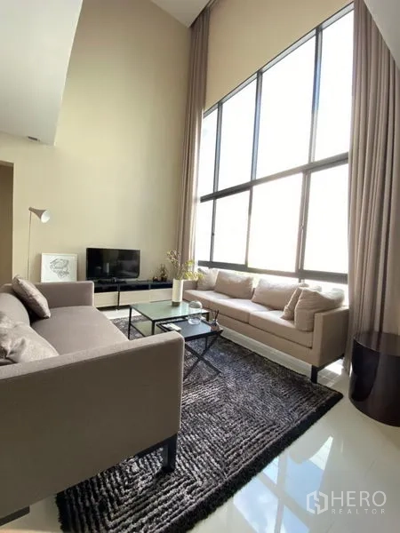 บ้าน ให้เช่าในHuai Khwang, Bangkok - ห้องนั่งเล่นเพดานสูงสองชั้น ผนังกระจกเต็มบาน โซฟา พรม โต๊ะกลาง และทีวี